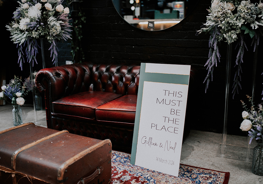 Moodily-lit room with chesterfield sofa, chest and welcome sign that reads "This must be the place"